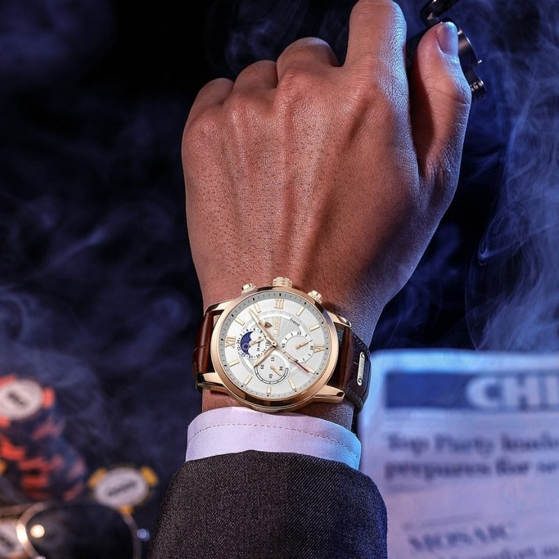 Aurelius Timepiece men's watch with gold case, white dial, and brown leather strap on a man's wrist in a dark setting.