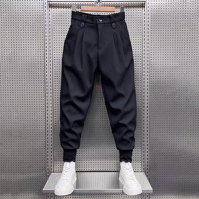 Full view of black pleated harem trousers with elasticated cuffs, displayed on a mannequin with white sneakers.
