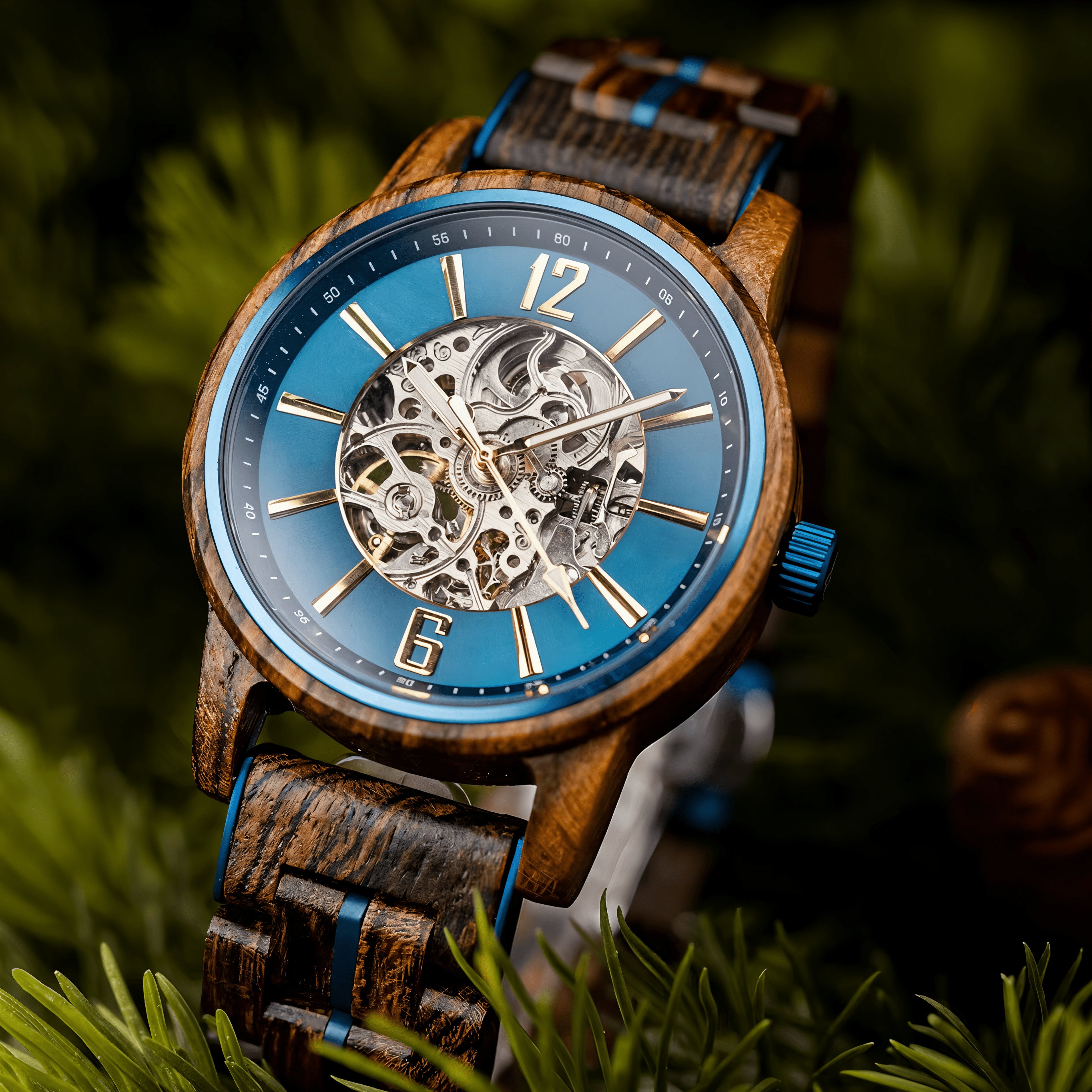 Cascadia Blue men's wooden watch with stainless steel accents, featuring a blue skeleton dial and dark wood strap with blue details, resting on vibrant green pine needles.