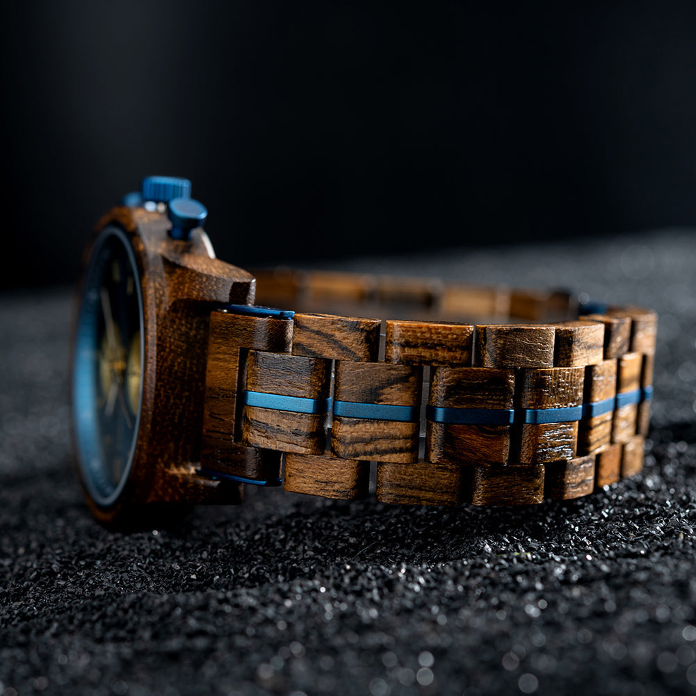 Close-up side view of the Celestial Oak Men's Wooden Watch, highlighting the wooden strap with blue accents, resting on a dark, granular surface.