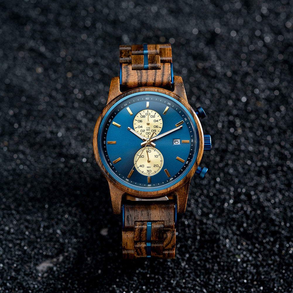 An overhead view of the Celestial Oak men's wooden watch, showcasing its blue dial with gold subdials and wooden strap with blue accents, placed on a dark, textured surface.