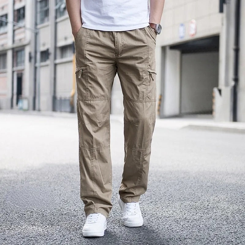 Front view of a man wearing khaki Coastal Retreat cargo pants with utility pockets and white sneakers, standing on a street.