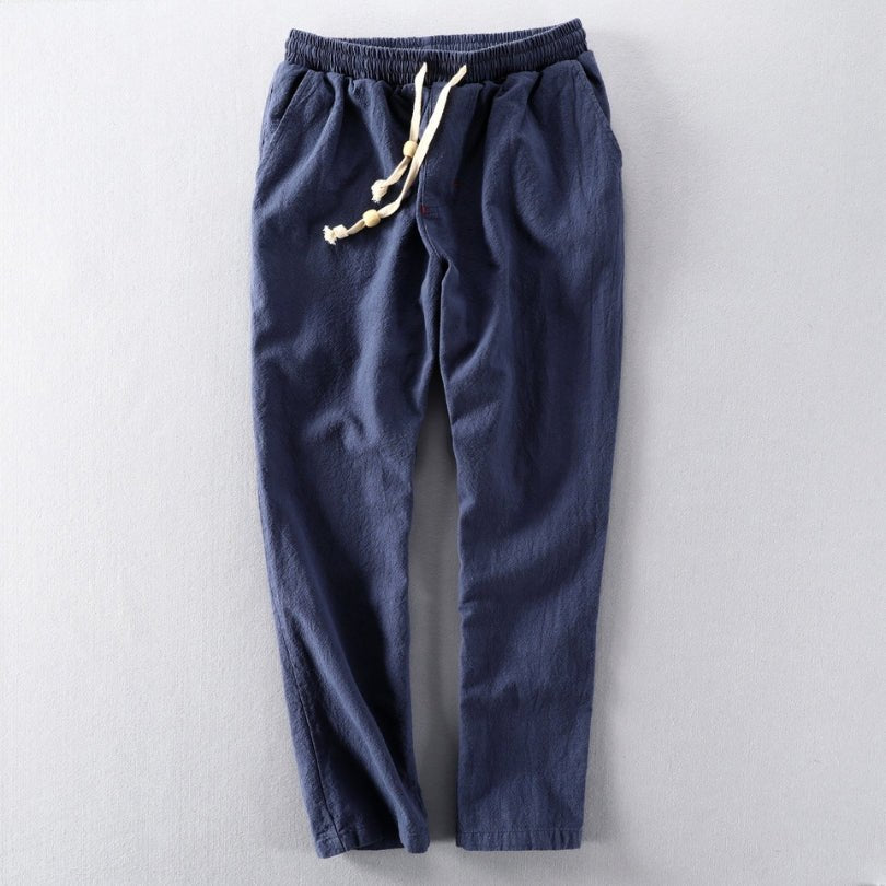 A pair of blue Edo Escape Japan-style linen trousers, laid flat on a light gray background, featuring a relaxed fit, elastic waistband, and a contrasting cream-colored drawstring.