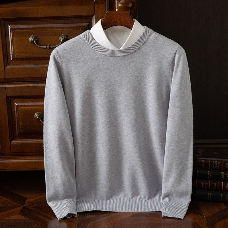 A light gray cashmere crewneck sweater layered over a white collared shirt, displayed on a wooden hanger against a dark wooden dresser.