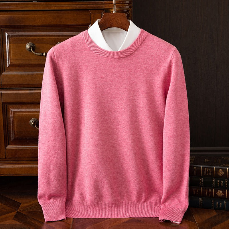 A vibrant pink cashmere crewneck sweater layered over a white collared shirt, displayed on a wooden hanger against a dark wooden dresser.