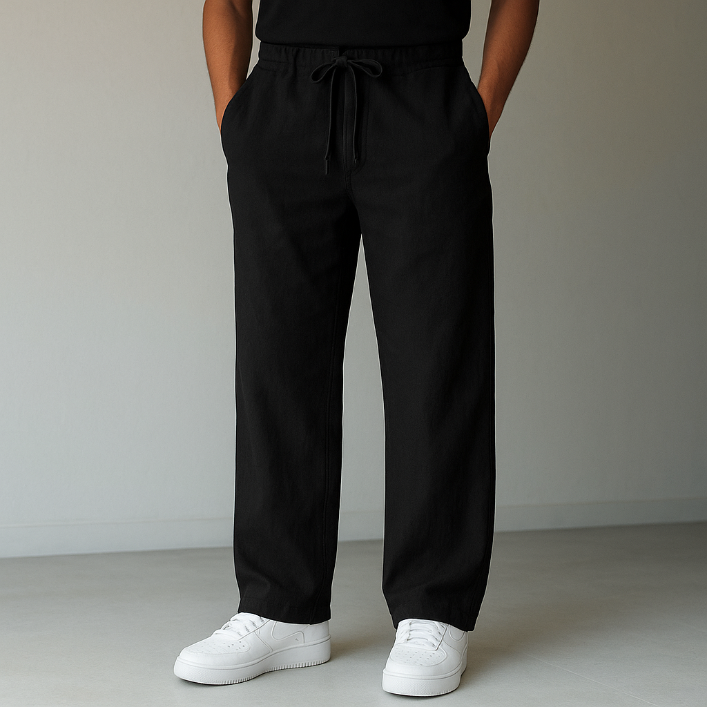 A person models black Elysian Breeze linen pants with a relaxed fit, featuring a drawstring waist, paired with white sneakers against a minimalist background.