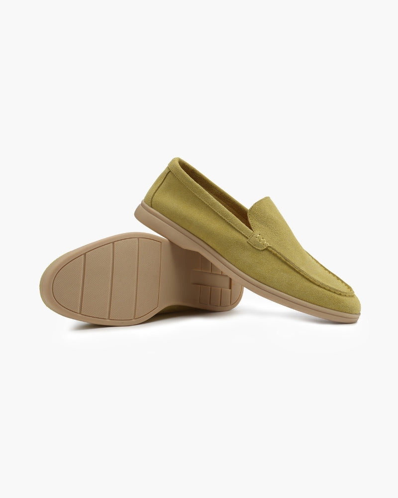 A pair of light green suede men's loafers, one standing upright showing the side and top, the other on its side revealing the tan sole with a grip pattern, against a white background.
