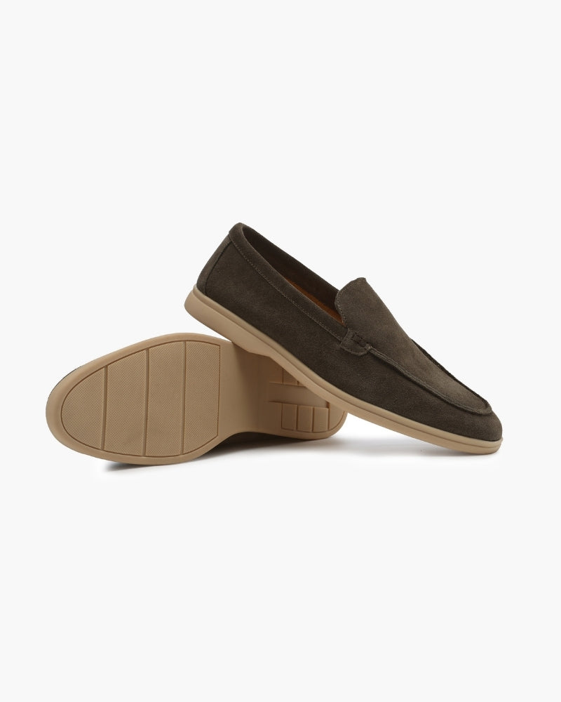 Pair of Heritage Luxe men's olive green suede loafers with classic stitching, one lying on its side revealing the textured sole, on a plain background.