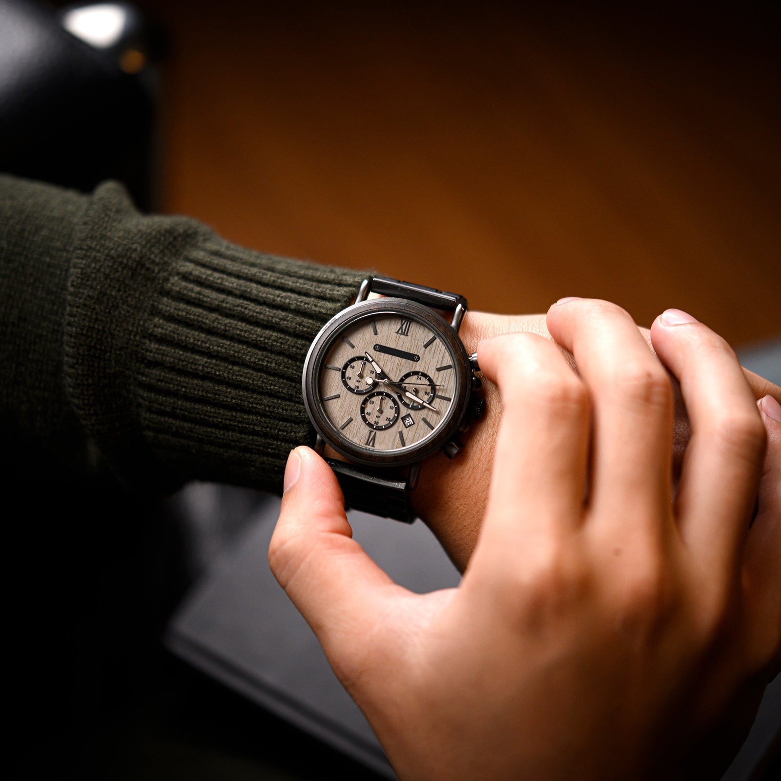 Heritage Oak men's watch with natural wood and dark metal strap worn on a man's wrist, showing the light dial and chronograph features, with a dark green sweater sleeve.