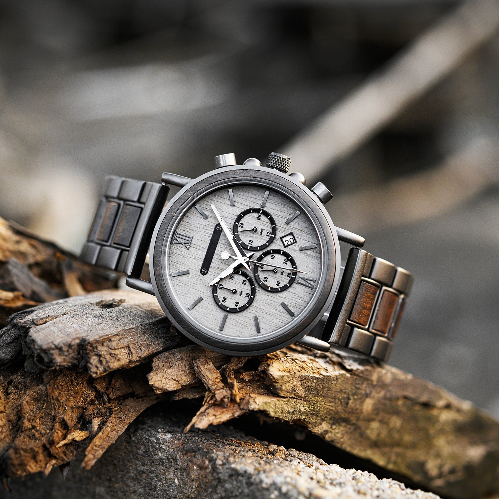 Heritage Oak men's watch with natural wood and dark metal strap, light dial, and chronograph features, displayed on a piece of weathered wood in an outdoor setting.