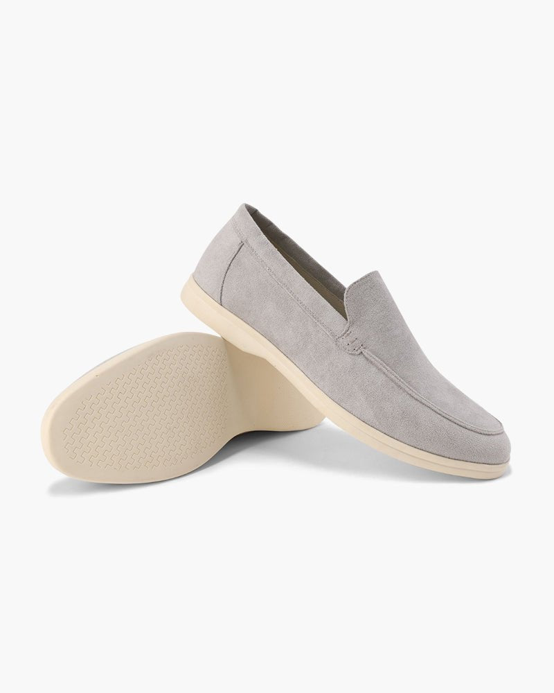 Pair of Heritage Luxe Light Gray suede loafers with classic stitching, one upright showing the top and side, the other on its side revealing the textured sole. White background.