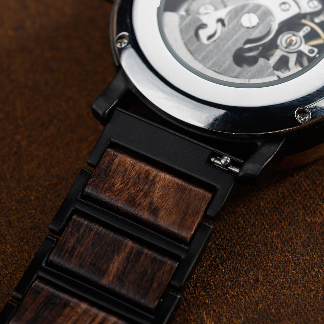 Extreme close-up Terra Brown men's wooden watch back, revealing exposed mechanical movement through clear case back dark brown wooden links strap.