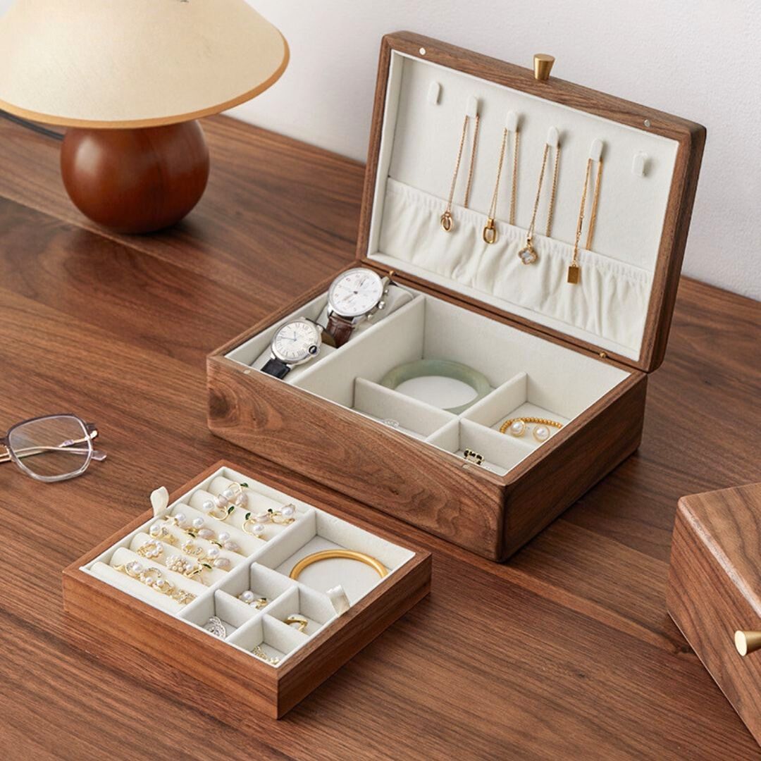 Open solid walnut wood jewelry box displaying watches, necklaces, and a jade bracelet, with a removable tray pulled out and filled with rings and earrings. Showcases the box's organization for men's accessories.