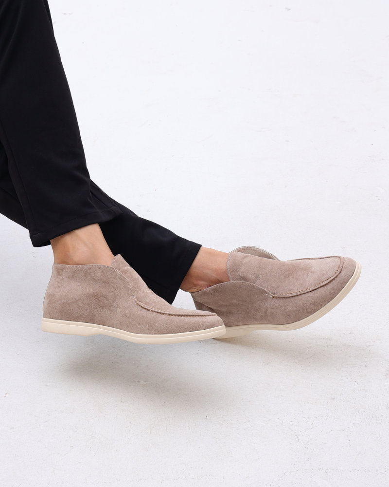 Side view of a person wearing beige suede loafers with classic detailing and black pants.