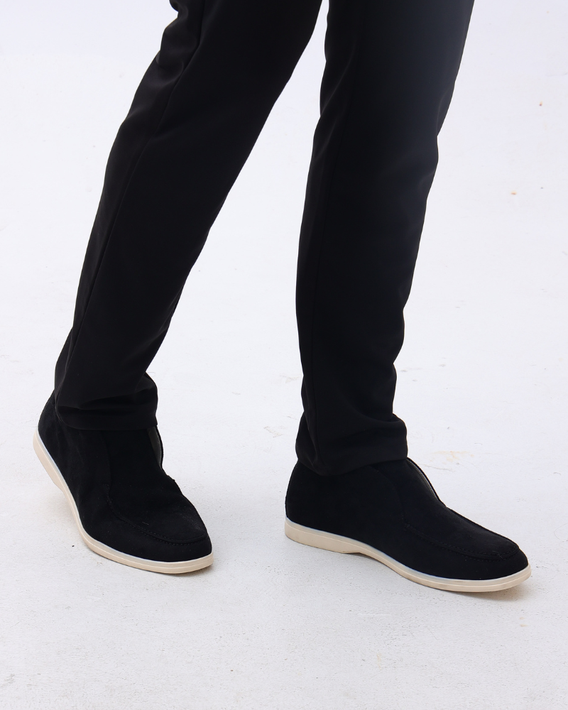 Close-up of a person wearing black suede loafers with classic detailing and black pants, shown from a front view.