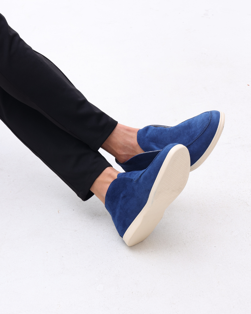 Marine blue suede loafers with classic detailing worn by a person in black pants, captured from a side view.