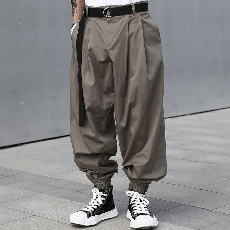 Urban Essence men's grey-green baggy pleated pants with a retro design, elastic cuffs, and a black belt, shown on a male model from the front.