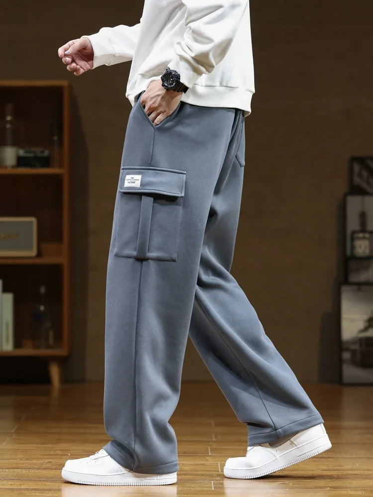 Urban Nomad dark gray cargo sweatpants made from soft cotton, featuring a relaxed fit and a large utility pocket on the side. Worn by a person with a hand in the pocket, showcasing the side profile.