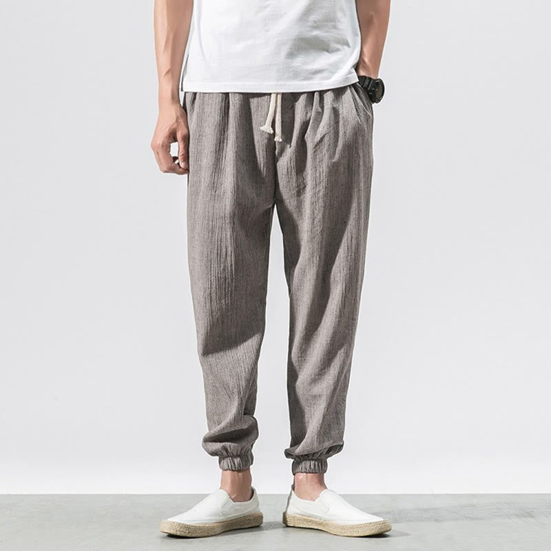 A man wearing Zenith Stones gray linen pants with a drawstring waist and side pockets, paired with a white t-shirt and white slip-on shoes.