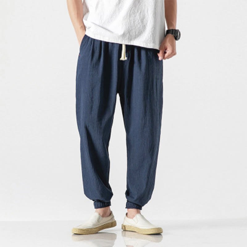 A man wearing Zenith Stones navy blue linen pants with a drawstring waist and side pockets, paired with a white t-shirt and beige slip-on shoes.