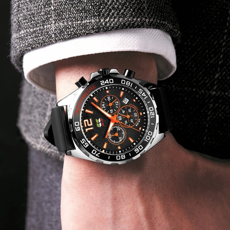 Apex Dusk men's quartz watch with luminous hands and date display, featuring a silver case, black dial with orange accents, and a black silicone strap, worn on a man's wrist with a grey suit jacket.