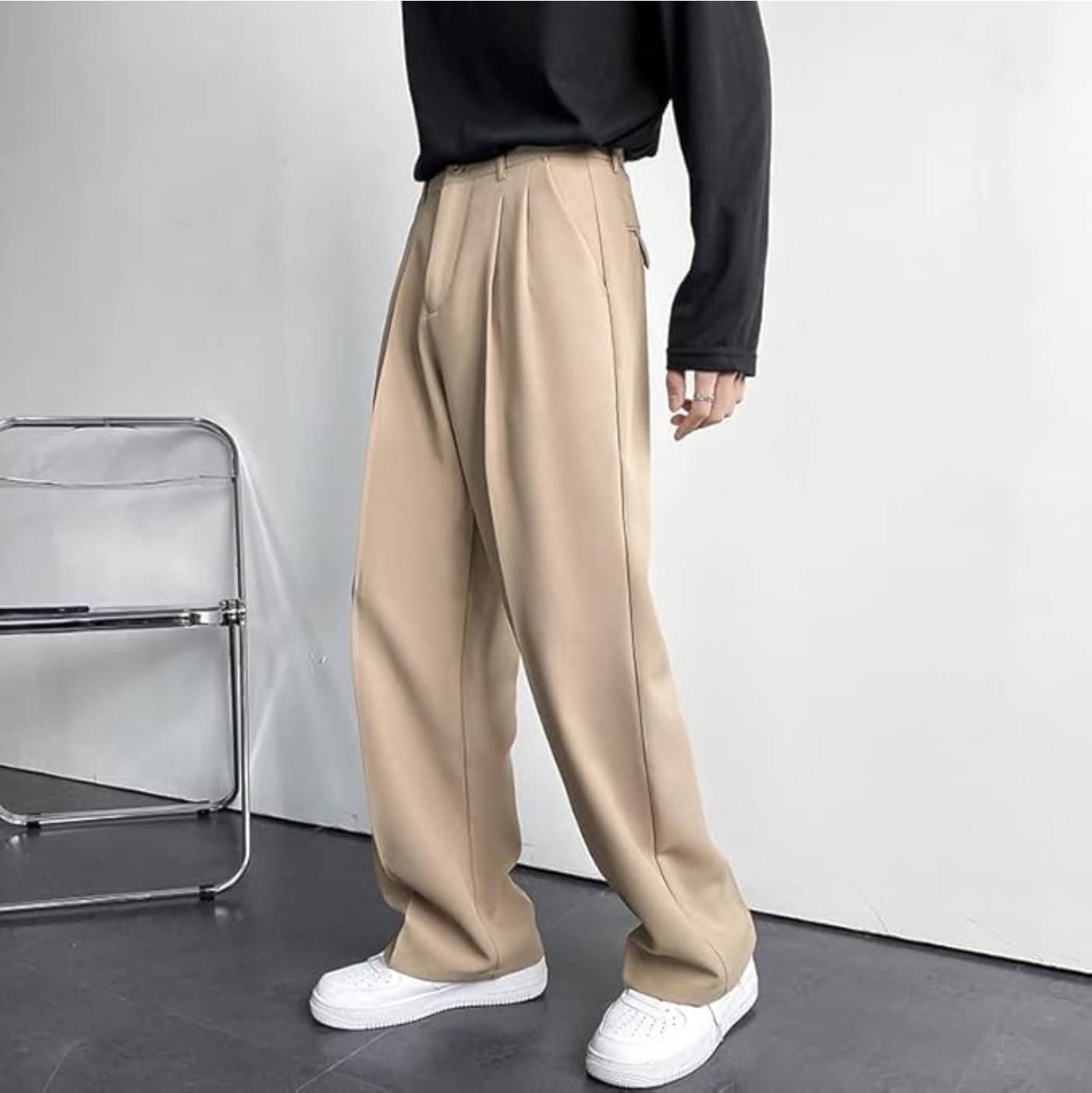 Men's Arno Trousers in beige linen, tailored fit, side view. Model showcasing pleated chinos with a black shirt and white sneakers.