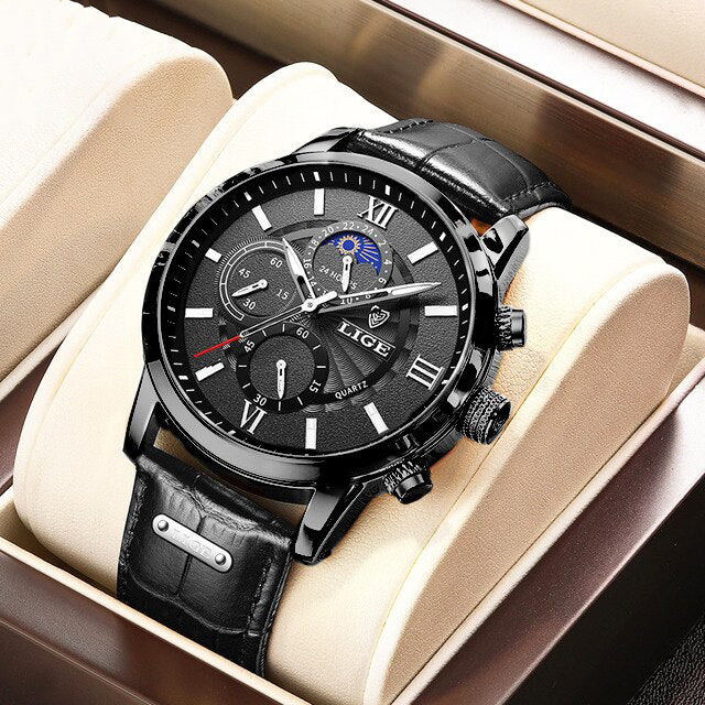 The Aurelius Timepiece men's watch in an all-black variant, featuring a black leather strap, black case, and black dial with Roman numerals and a moon phase, presented in a beige display box.