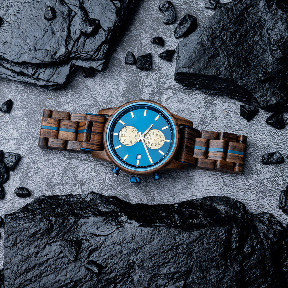 Celestial Oak Men's Wooden Watch with Blue Dial, shown from a top-down perspective, surrounded by dark, rough rocks on a grey textured surface.