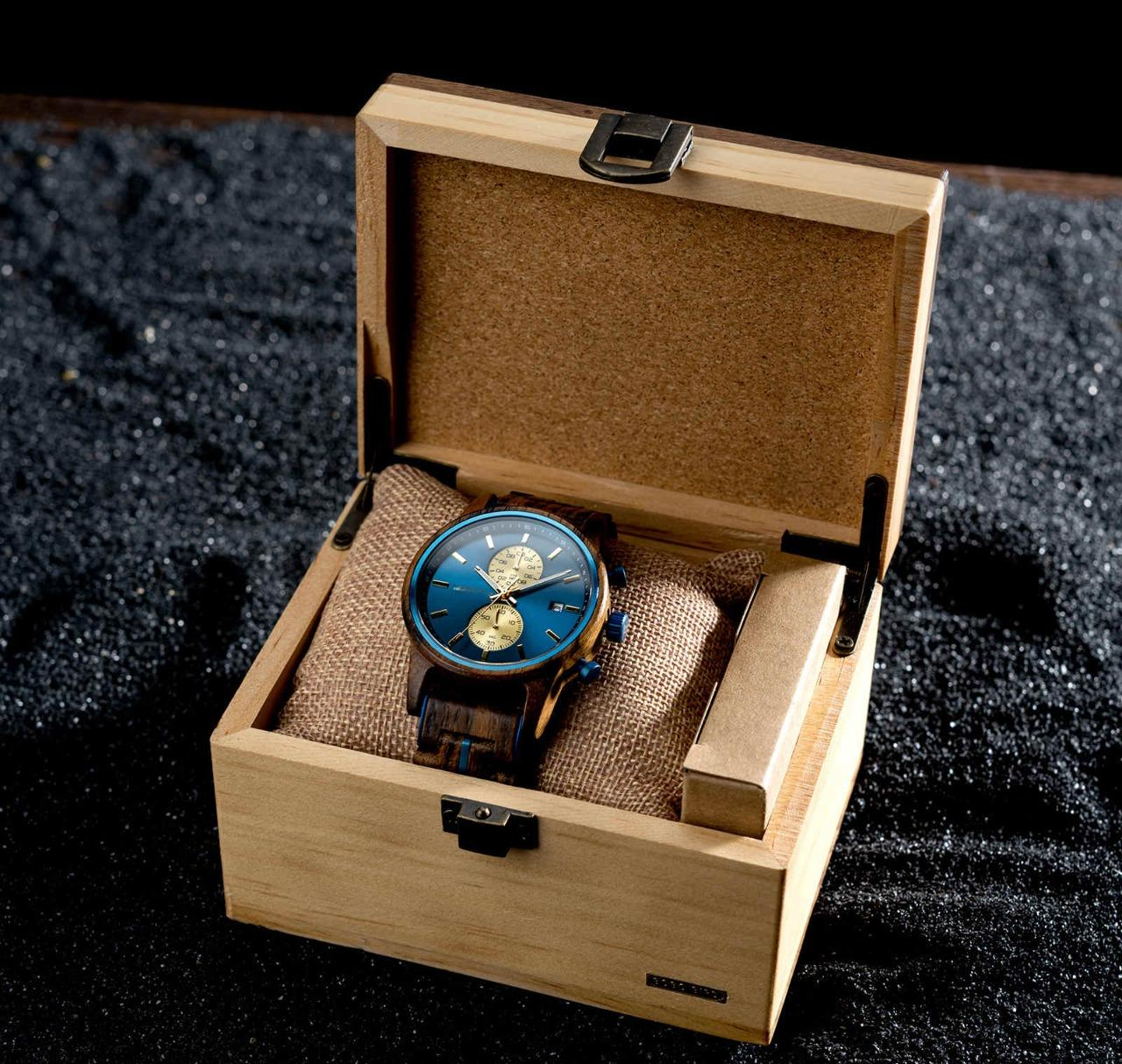 Celestial Oak Men's Wooden Watch with Blue Dial, displayed open in a light wooden presentation box, resting on a dark textured surface.