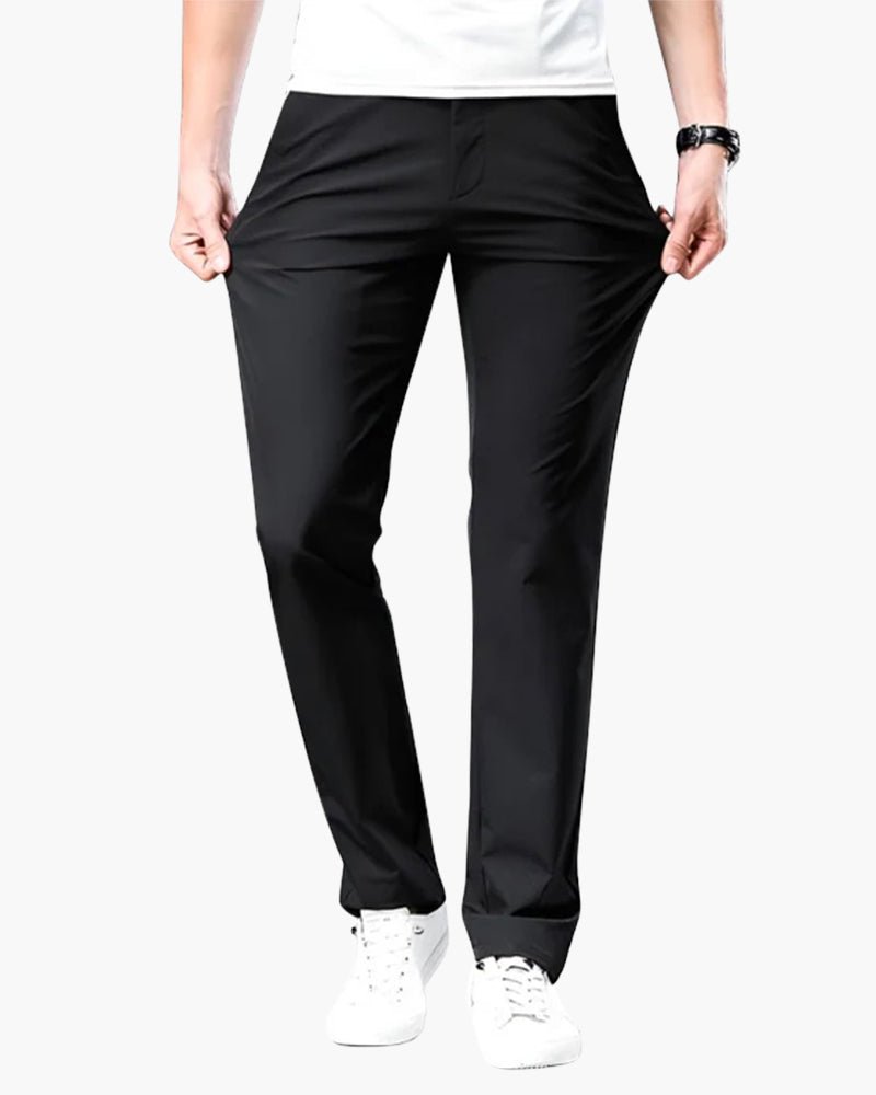 Men's Cielo Vento black casual trousers in lightweight cotton, shown on a model pulling the waistband to demonstrate the stretch fabric and relaxed fit. Paired with a white t-shirt and white sneakers.