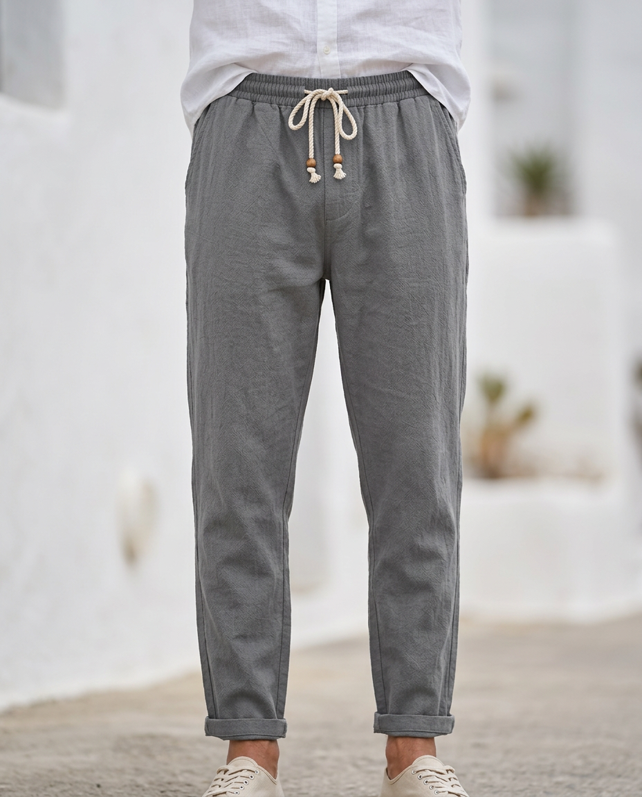 Men's Coastal Breeze dark gray linen trousers with a tailored fit, drawstring waist, and rolled cuffs, styled with a white shirt and light shoes on a cobblestone street.