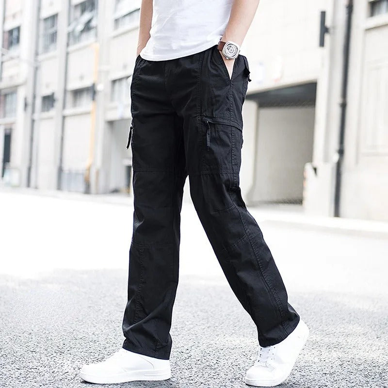 Male model wearing Coastal Retreat black cotton cargo pants with utility pockets and white sneakers, walking on a city street. The durable fabric and relaxed fit make them ideal for outdoor activities or everyday wear.