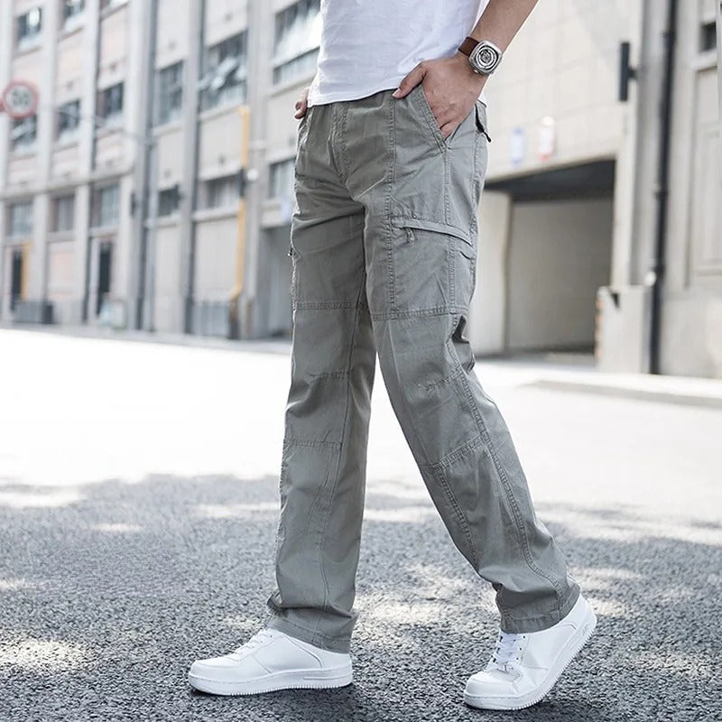 Male model wearing Coastal Retreat khaki cotton cargo pants with utility pockets and white sneakers, walking on a city street. These versatile pants are designed for comfort and casual style.