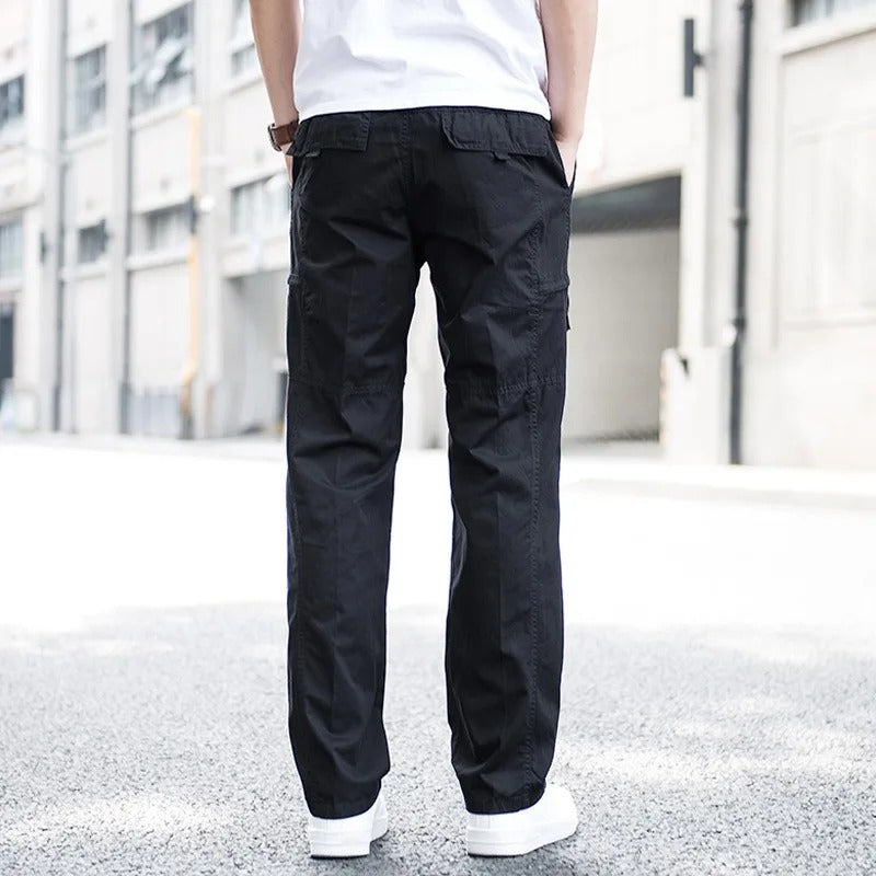 Back view of a man wearing black Coastal Retreat cargo pants with utility pockets and white sneakers, standing on a street.