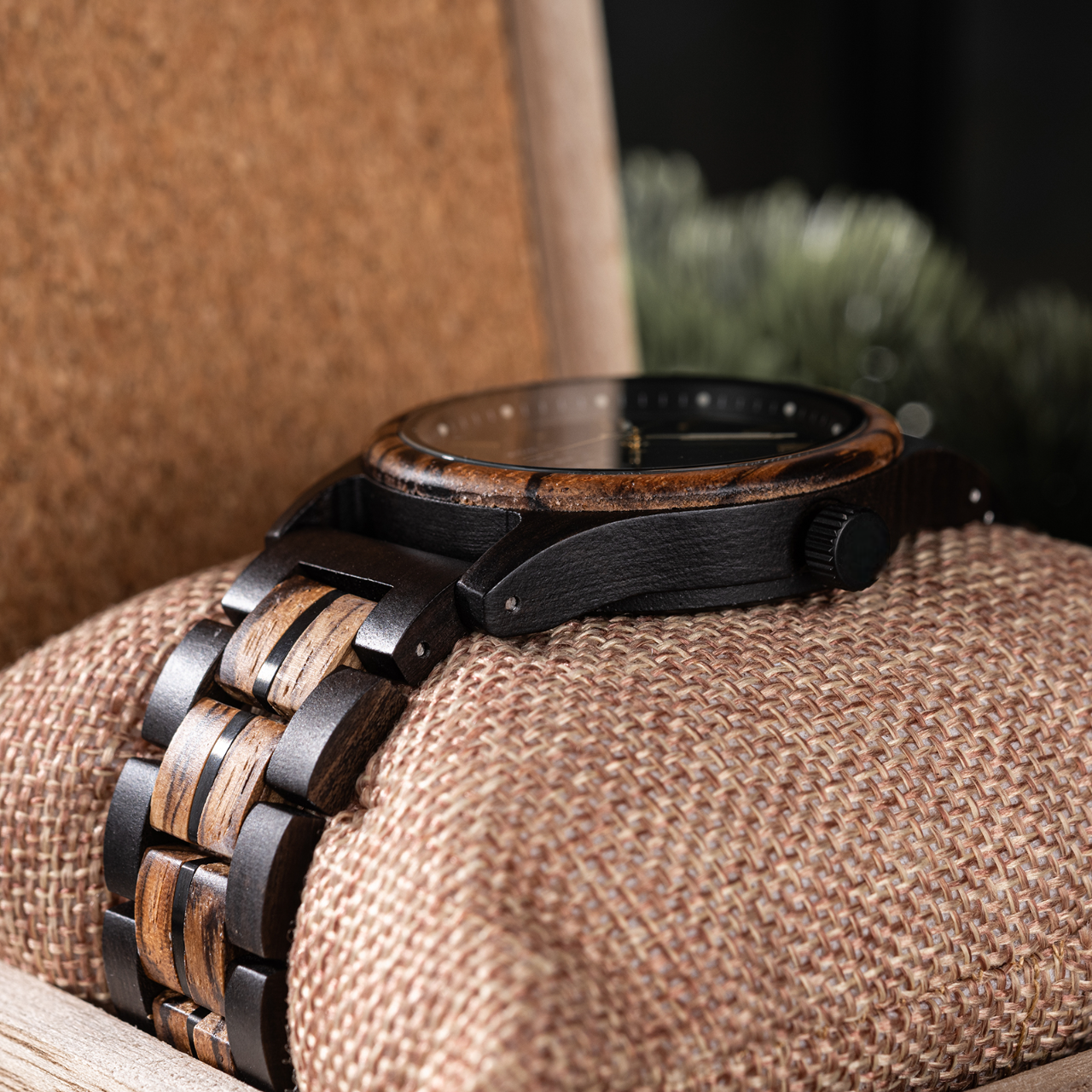 Side profile close-up of the Eclipse Noir men's watch, featuring a black stainless steel case, minimalist dial, and a two-tone dark and light wood strap, resting on a fabric cushion in a wooden box.