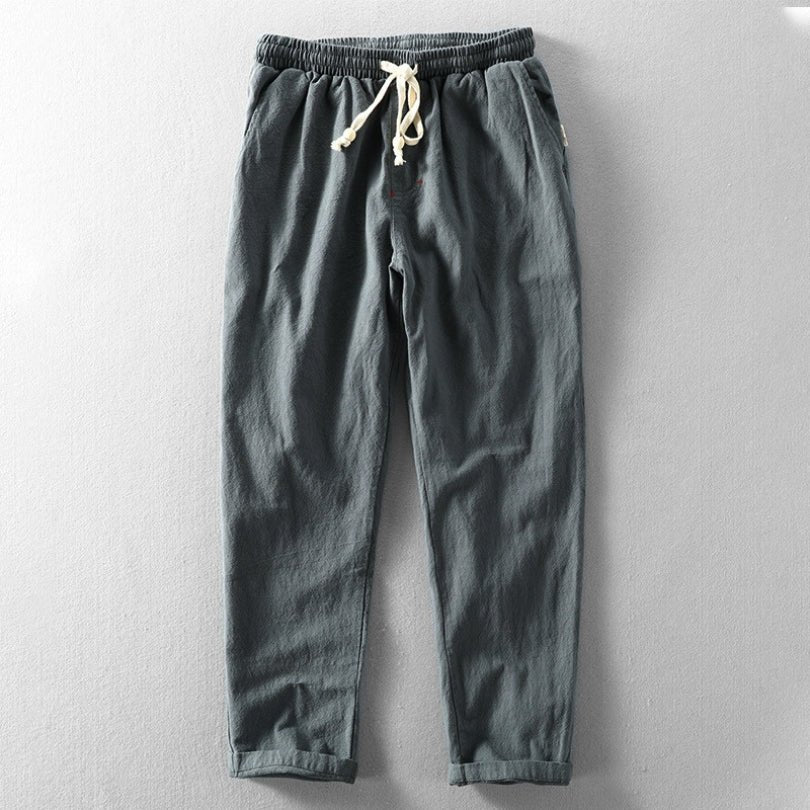 A pair of charcoal gray Edo Escape Japan-style linen trousers, laid flat on a light gray background, featuring a relaxed fit, elastic waistband, and a contrasting cream-colored drawstring.