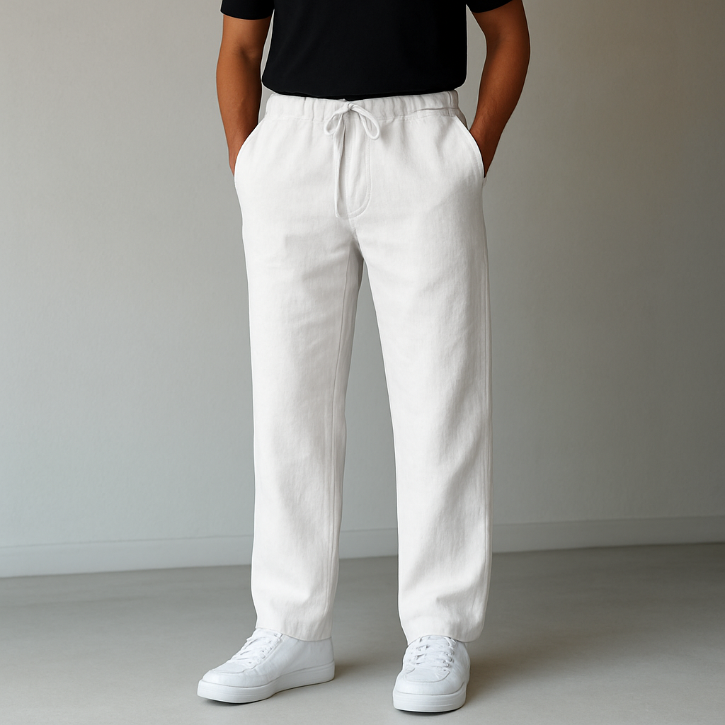 Full-body shot of a male model wearing white Elysian Breeze linen trousers with a relaxed fit and drawstring waist, paired with a black t-shirt and white sneakers.