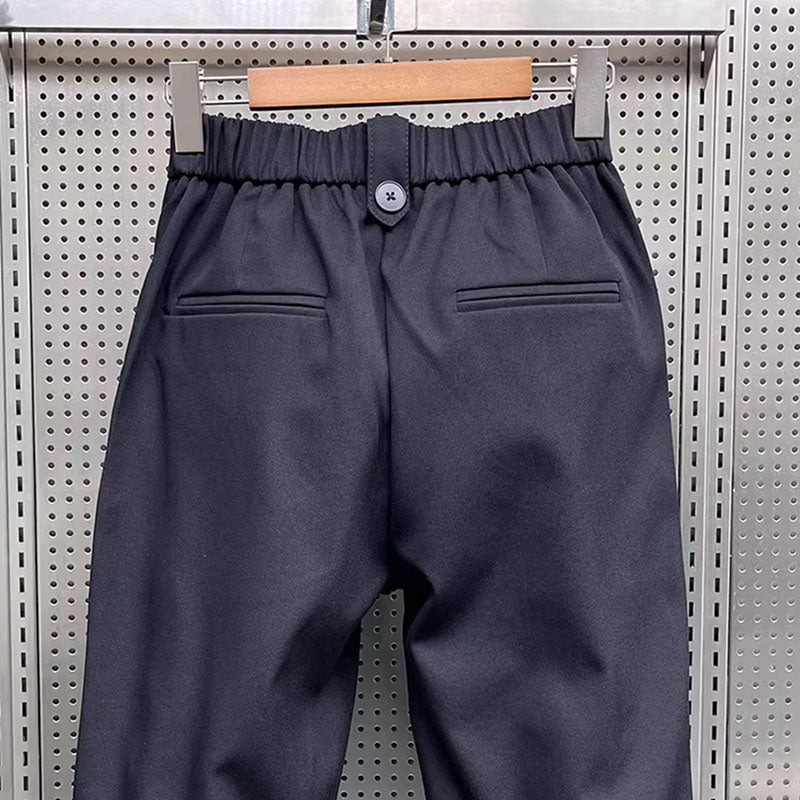 Close-up back view of black pleated harem trousers, highlighting the elasticated waistband, single button, and back pockets.