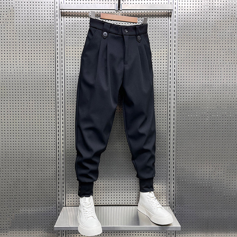 Front view of black pleated harem trousers with a relaxed fit and elasticated cuffs, displayed hanging with white platform sneakers.