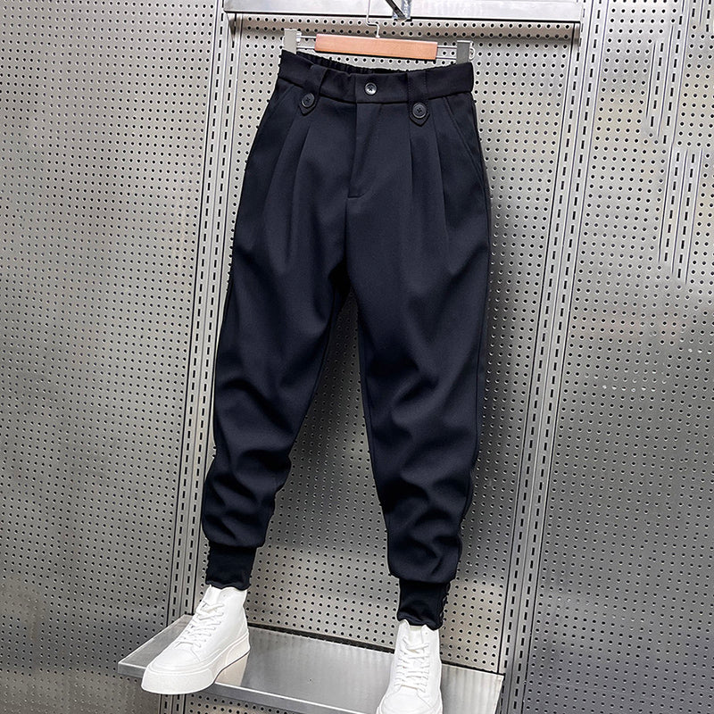 Black pleated harem trousers with a relaxed fit and elasticated cuffs, displayed hanging with white platform sneakers.