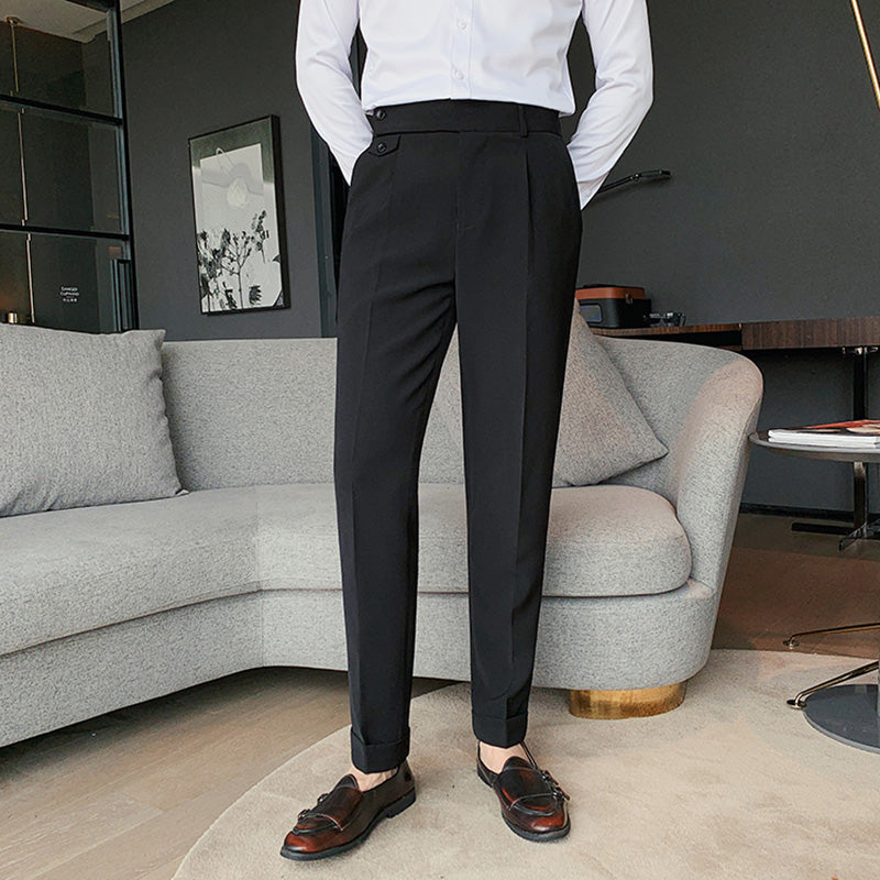 A man stands in an indoor setting, showcasing Elysian high-waisted slim-fit trousers in black. He wears a white shirt and dark loafers, highlighting the versatile and tailored look of the men's business wear.