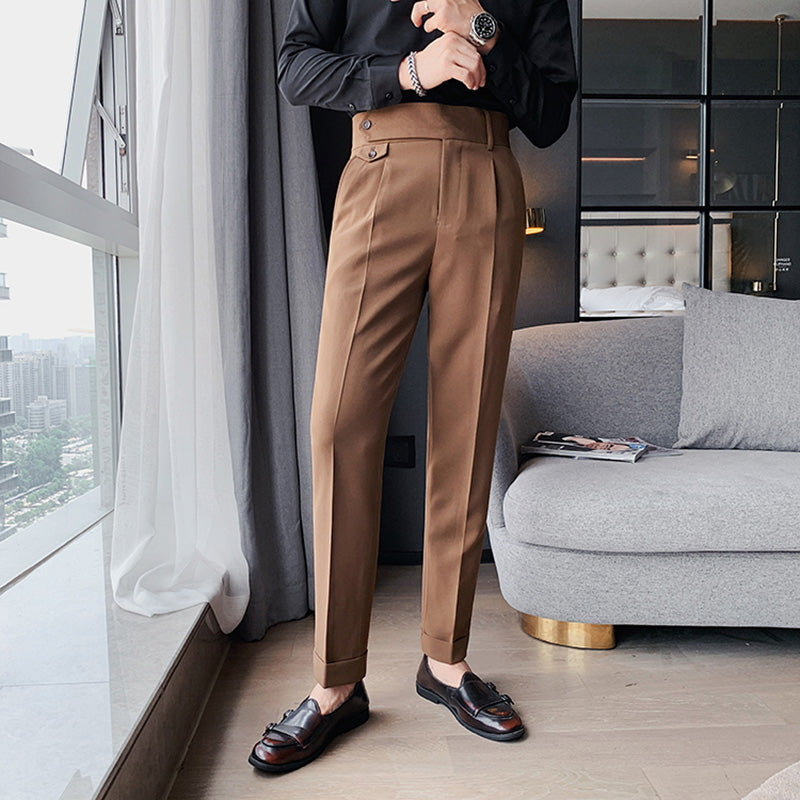 Full body view of a man modeling Elysian high-waisted slim-fit trousers in camel, paired with a black shirt and dark loafers. The trousers feature a tailored finish and are shown in a smart casual setting.