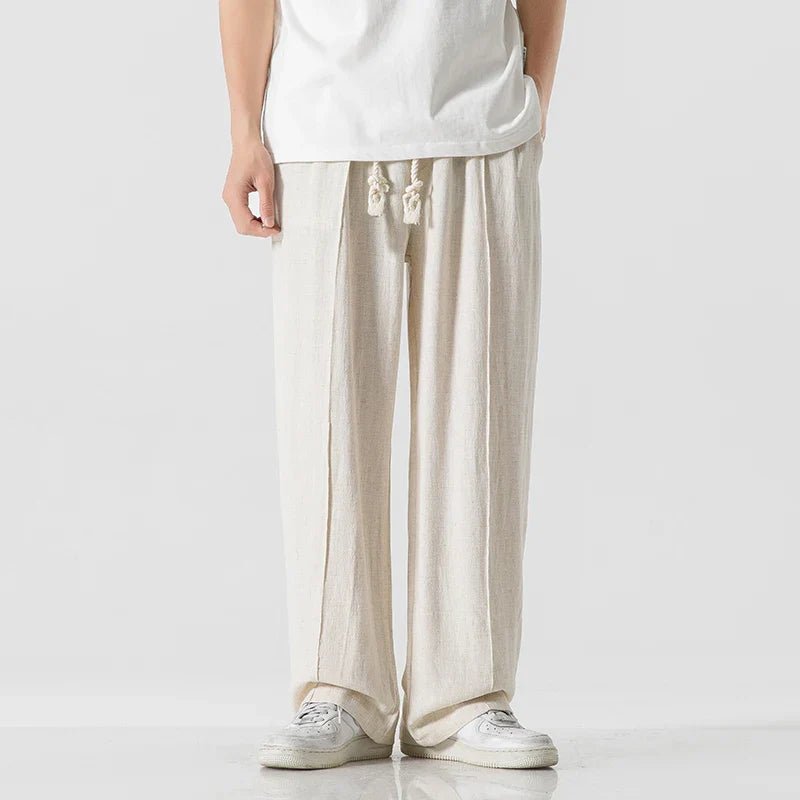 Elysium Drift beige linen sweatpants with a relaxed fit, shown on a male model from a front view, paired with a white t-shirt and white sneakers.