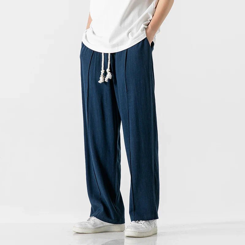 Elysium Drift blue linen sweatpants with a relaxed fit, shown on a male model from a side view, paired with a white t-shirt and white sneakers.