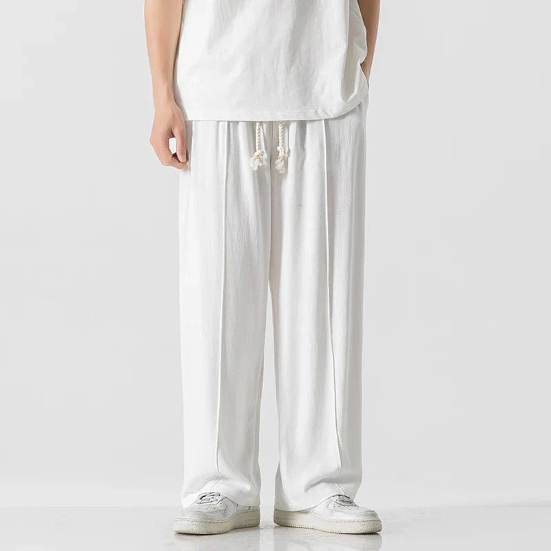Elysium Drift white linen sweatpants with a relaxed fit, shown on a male model from a front view, paired with a white t-shirt and white sneakers.