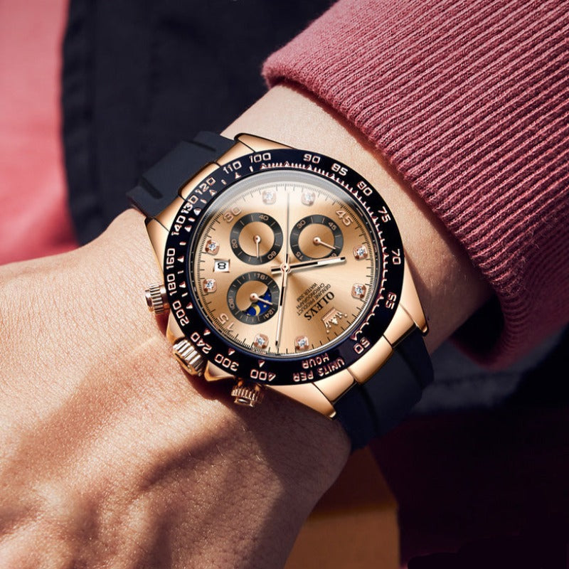 A man's wrist wearing an Elysium Timepiece watch with a champagne dial, rose gold-tone case, black silicone strap, quartz movement, and luminous hands, against a red sweater.