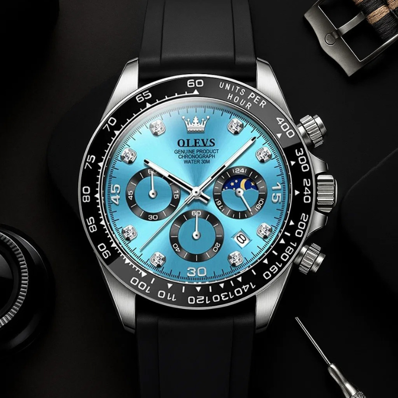 Overhead shot of the Elysium Timepiece men's watch with a blue dial, diamond-like markers, and a black silicone strap, displayed on a dark surface with watch adjustment tools.