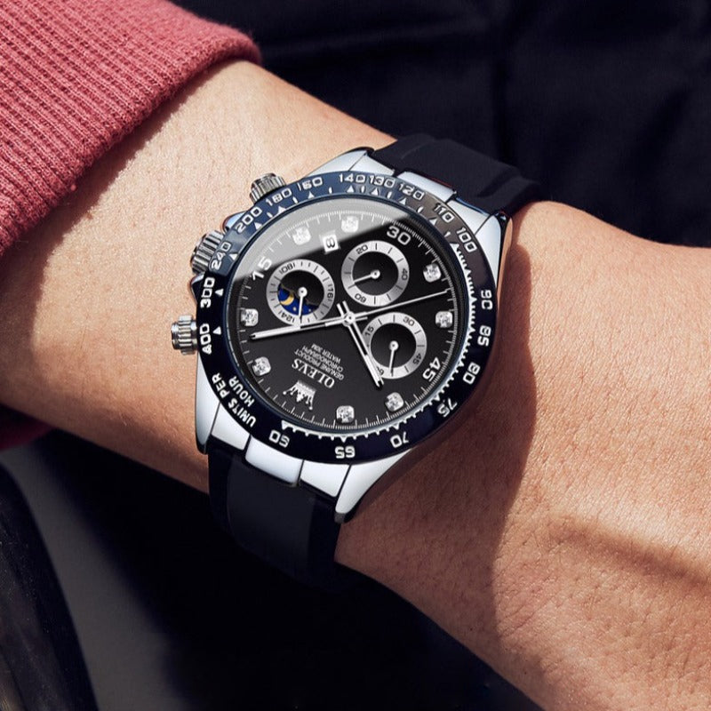 Men's Elysium Timepiece watch with quartz movement and luminous hands, featuring a silver case, black dial, and black silicone strap, worn on a man's wrist.