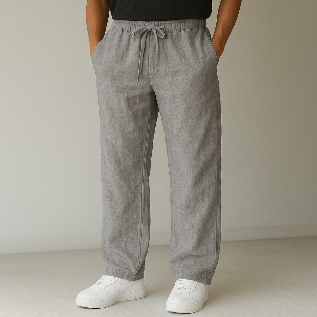 A person models gray Elysian Breeze linen pants with a relaxed fit, featuring a drawstring waist, paired with white sneakers against a minimalist background.