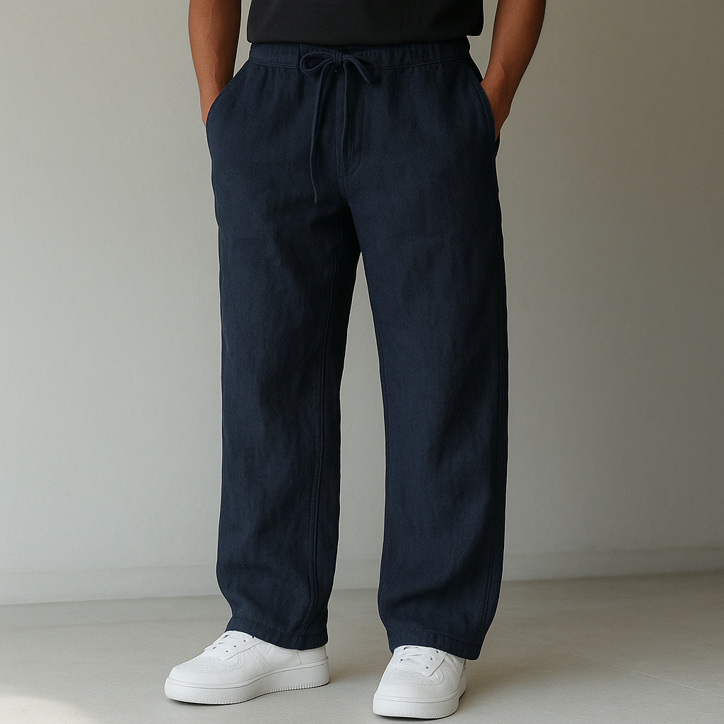 A person models navy Elysian Breeze linen pants with a relaxed fit, featuring a drawstring waist, paired with white sneakers against a minimalist background.